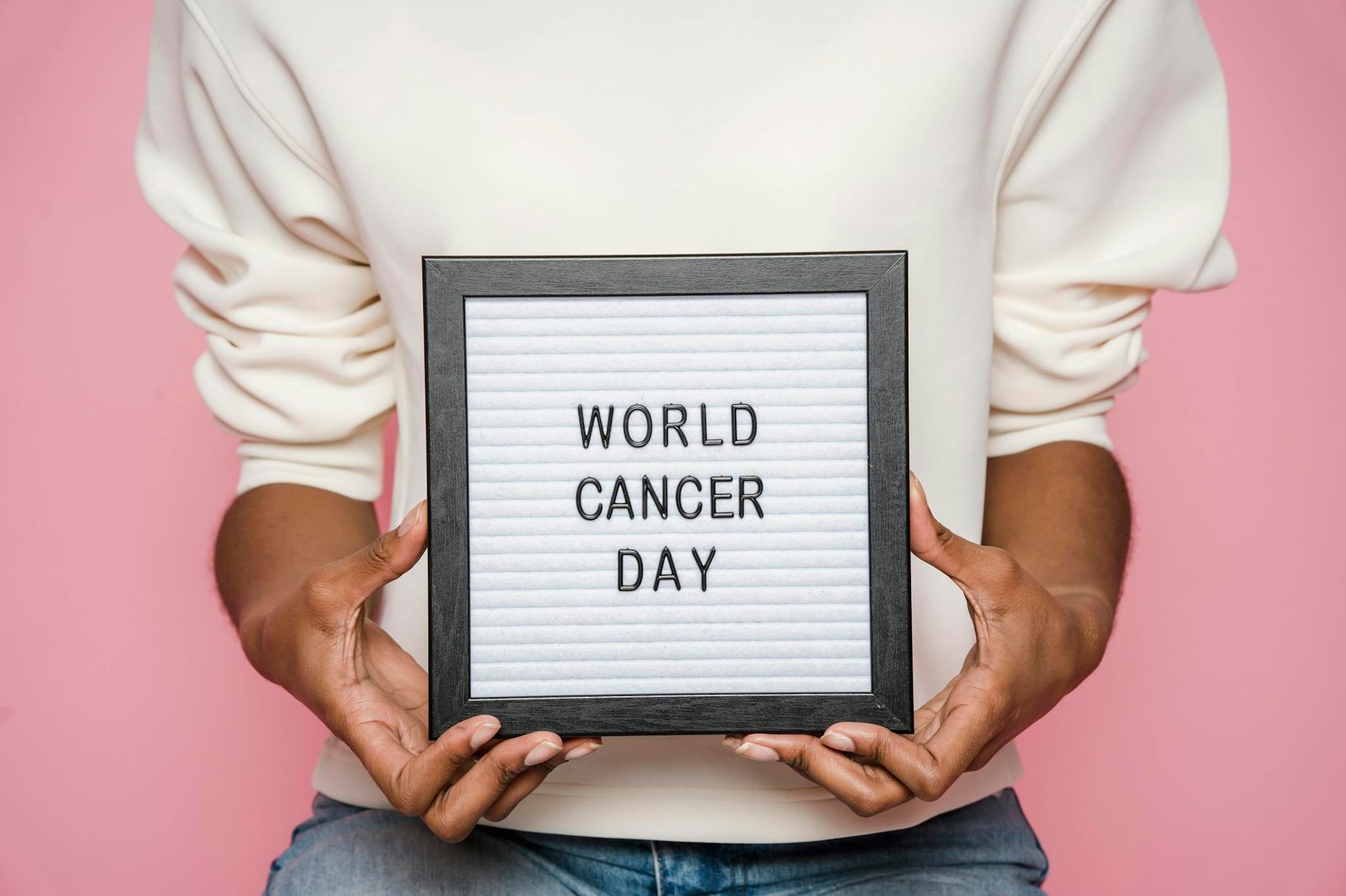 A person holding a letter board displaying 'World Cancer Day' against a pink background.
