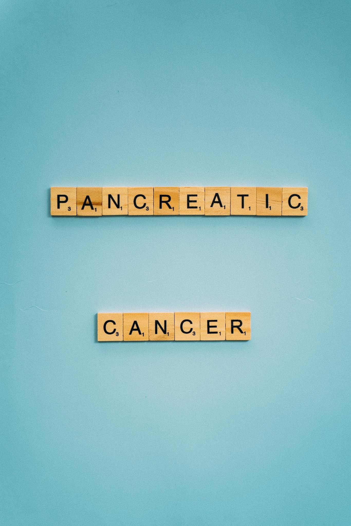 Scrabble tiles spelling pancreatic cancer on a blue background for awareness.