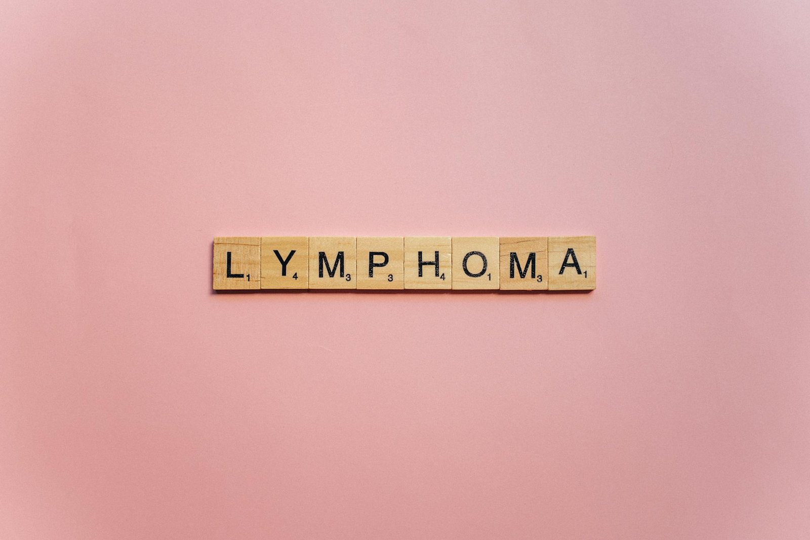 Wooden letter tiles spelling 'Lymphoma' on a pink background, symbolizing awareness.