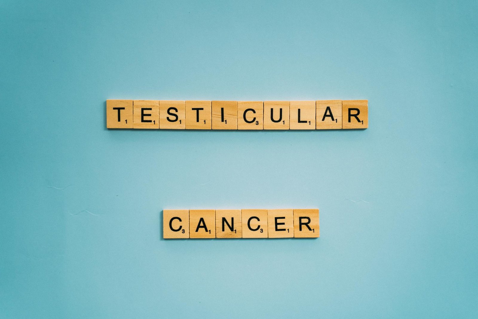 Wooden letter tiles spelling testicular cancer on a blue background, concept photo.